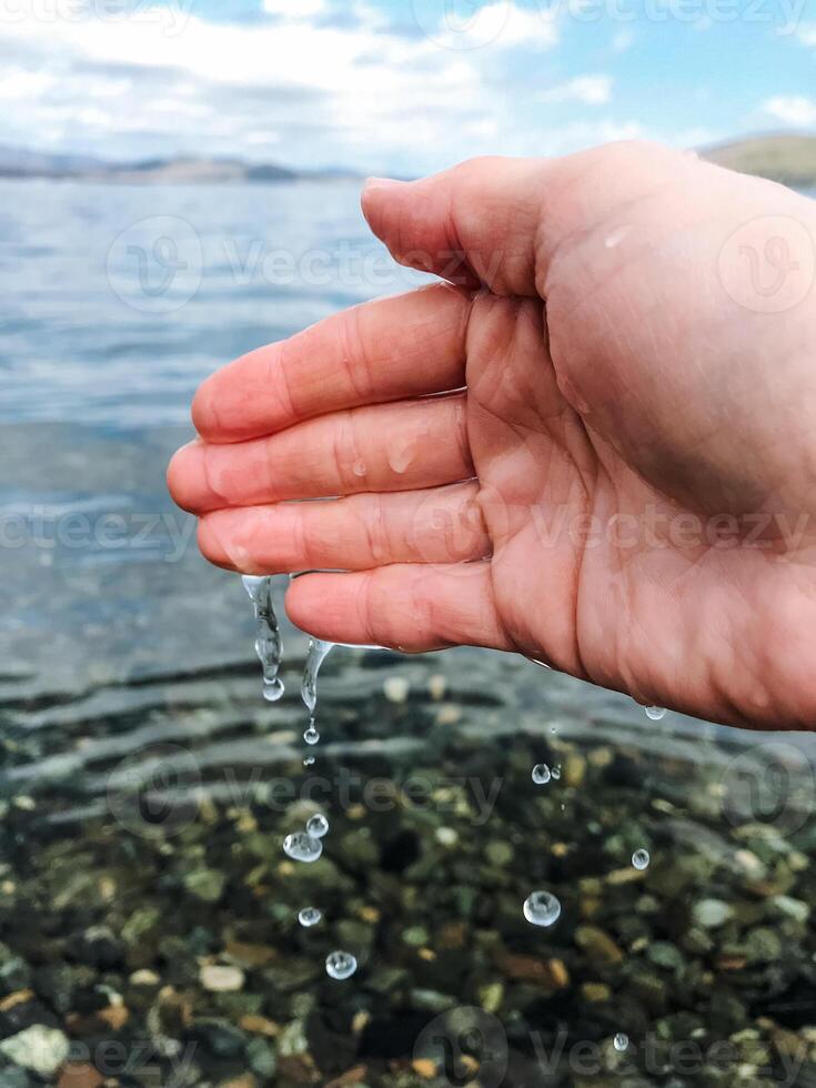 A persons hand is carefully reaching out toward a beautiful body of water, hoping to touch its smooth surface or perhaps feel a gentle wave lapping against their fingers photo