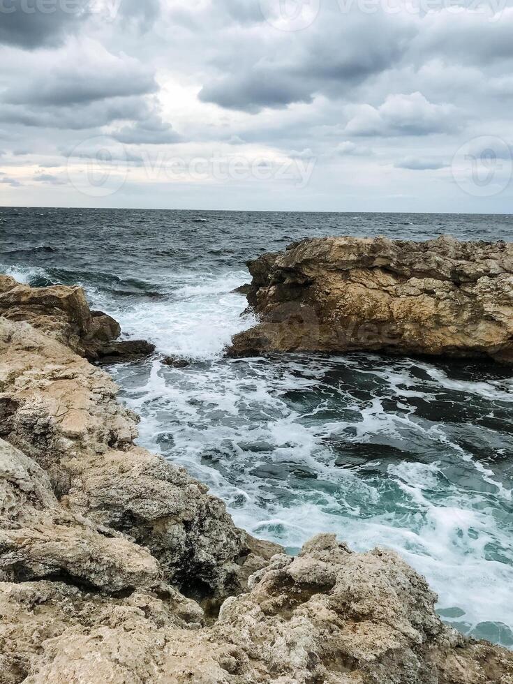 A picturesque rocky shoreline where waves crash powerfully against the large rocks on an overcast, cloudy day filled with a gray sky and a feeling of natures raw beauty photo