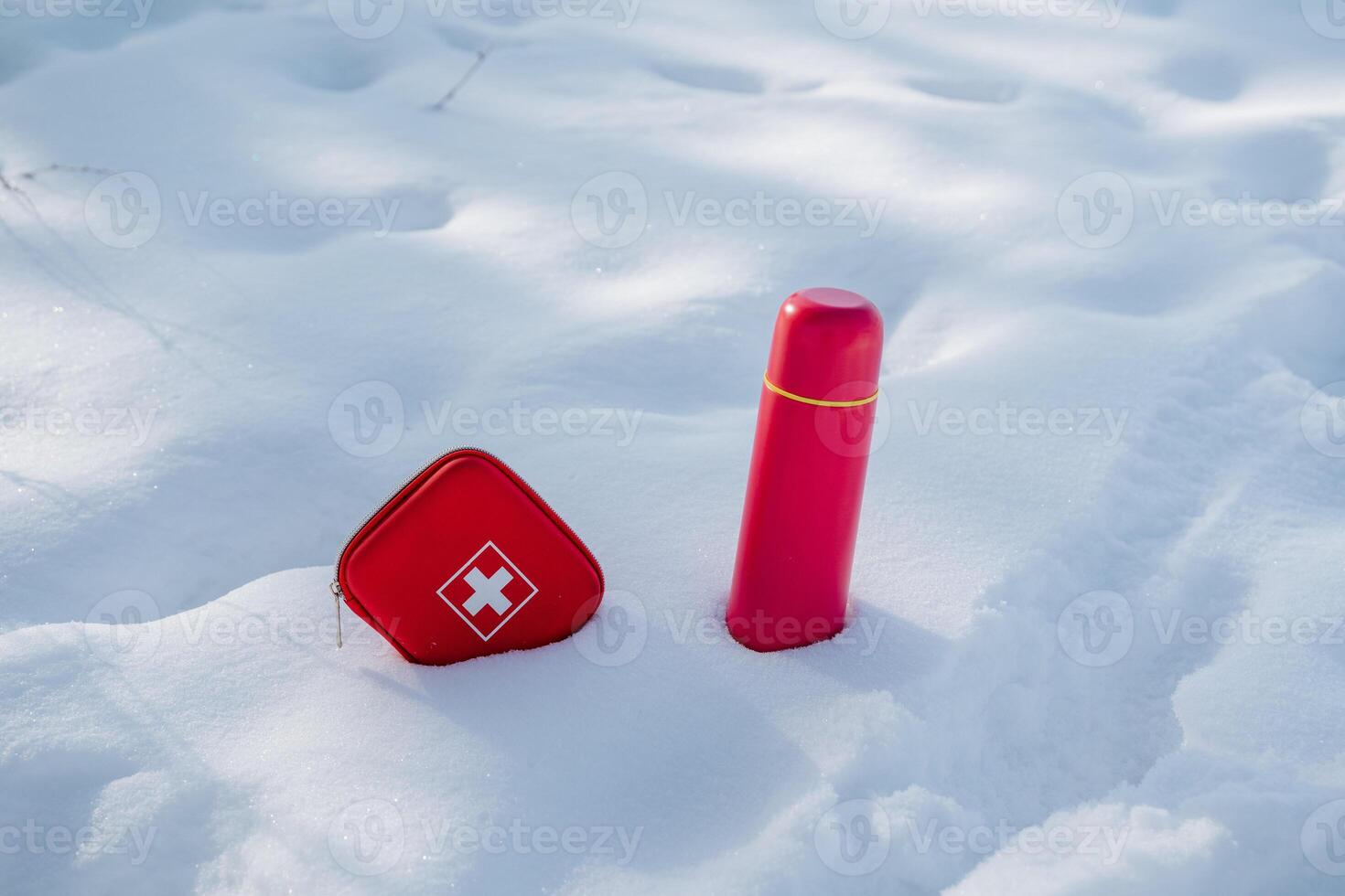 In the vast, snowy landscape, a bright red first aid kit and a vibrant red thermos provide an eyecatching and striking contrast against the pure, unblemished white backdrop of snow and ice photo