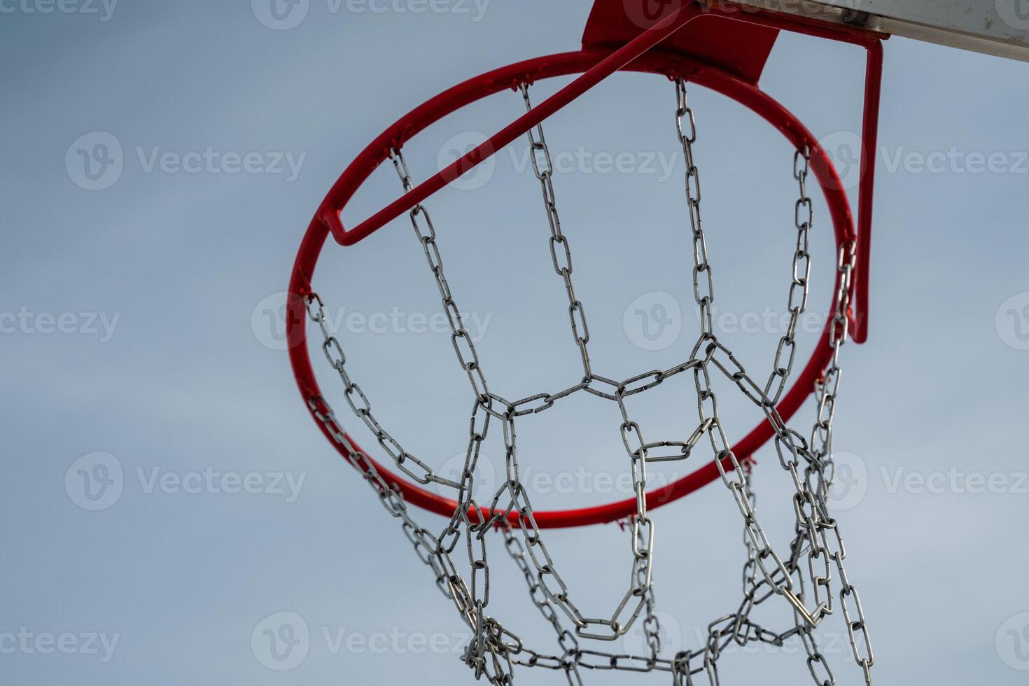 This is a closeup view of a basketball hoop, featuring chains, set against the backdrop of a clear blue sky. It highlights the essence of athletic activity and recreation photo