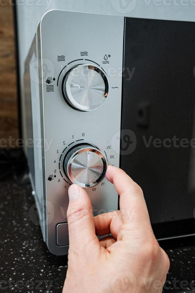 A person is actively pressing a button on a microwave oven, which is a highly popular kitchen appliance renowned for its ability to quickly heat and cook a variety of foods with efficiency photo