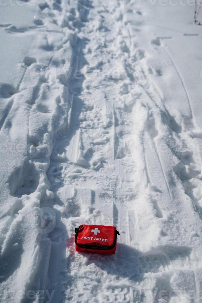 A vibrant red first aid kit is prominently positioned amidst the cold, white snow, beautifully contrasting against the vast and serene winter landscape that surrounds it photo