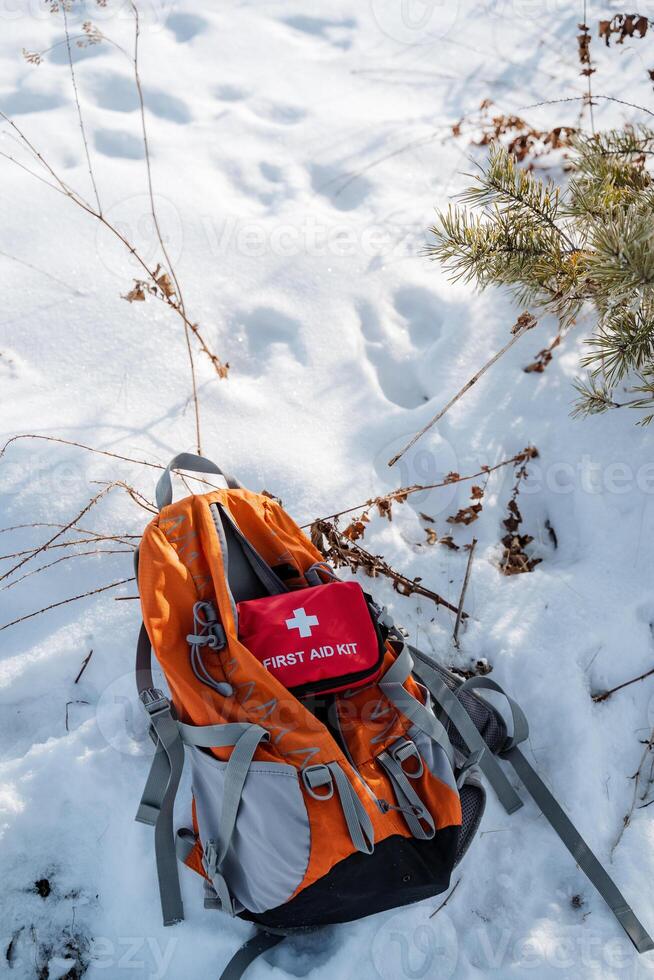 A backpack that contains a fully stocked first aid kit is currently laying abandoned in the snow, likely forgotten or misplaced, waiting to be discovered by someone nearby photo