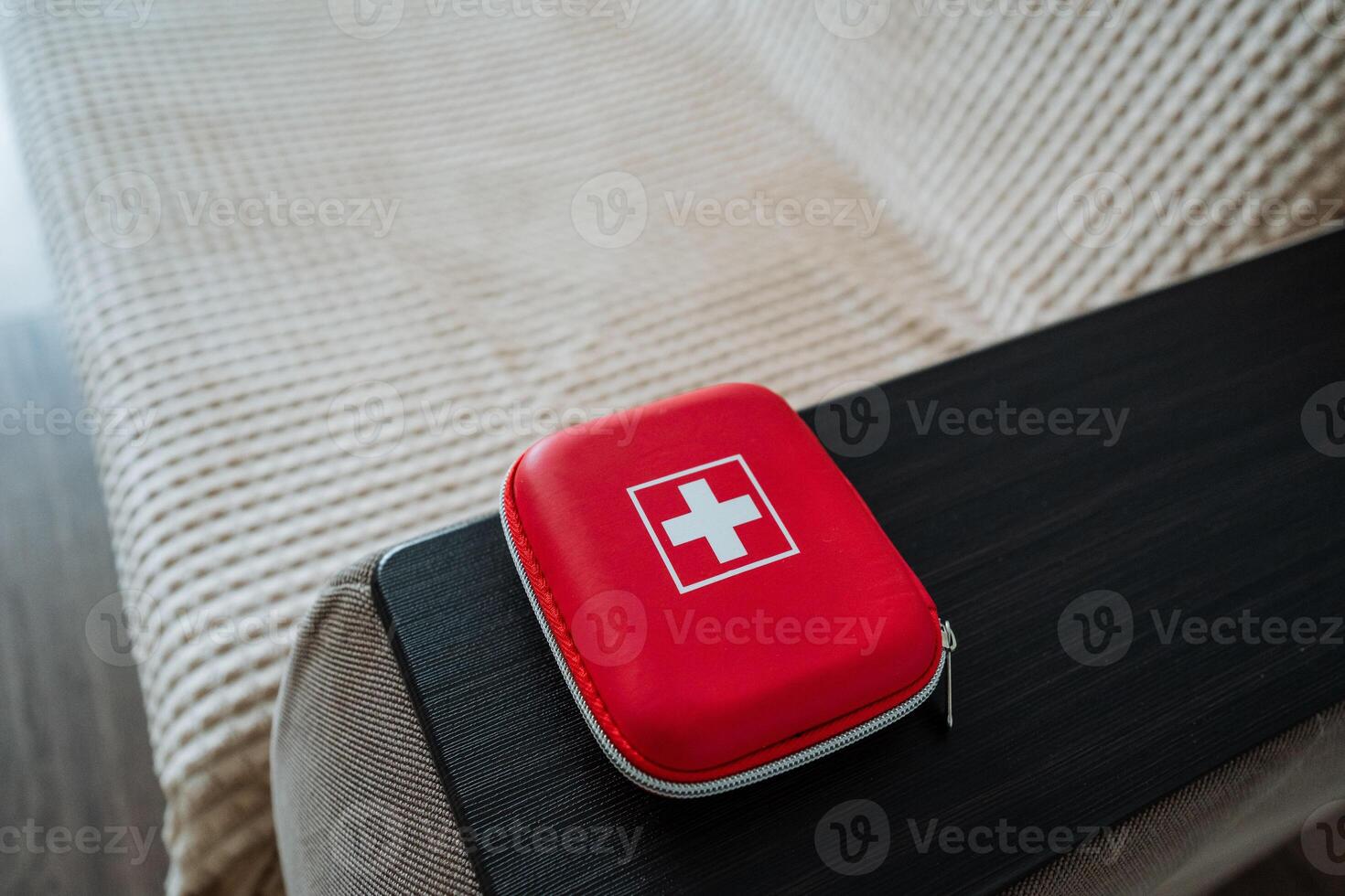 A red first aid kit, clearly marked with a prominent white cross emblem, is sitting neatly on a bed, ready to assist in case of any minor injuries or emergencies that may occur photo