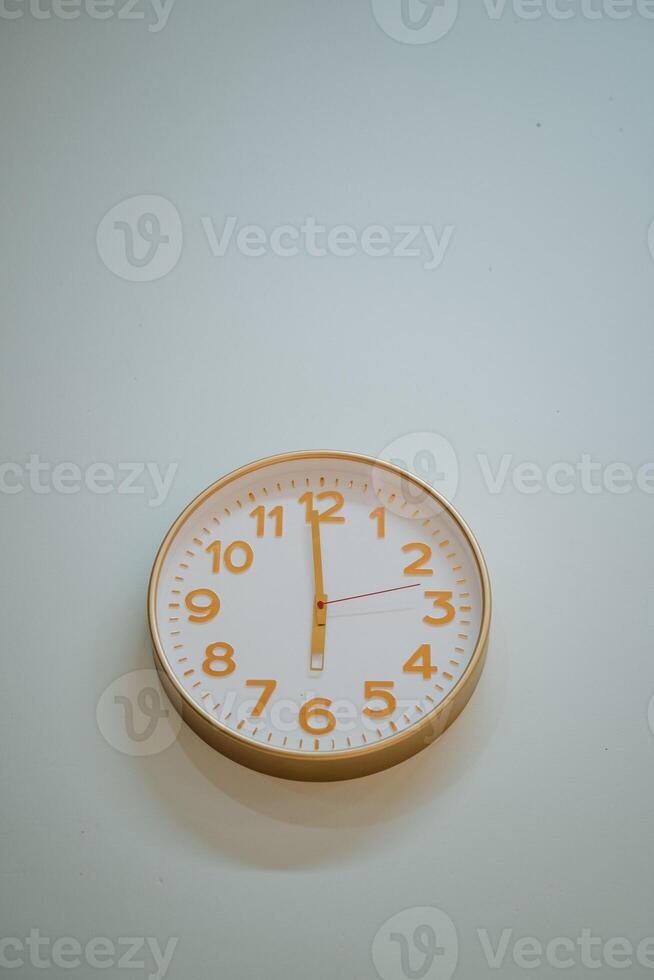 A beautifully designed round clock placed upon a spotless white wall shows that the time is swiftly approaching 500 PM, indicating that the day is gradually shifting into the evening hours photo