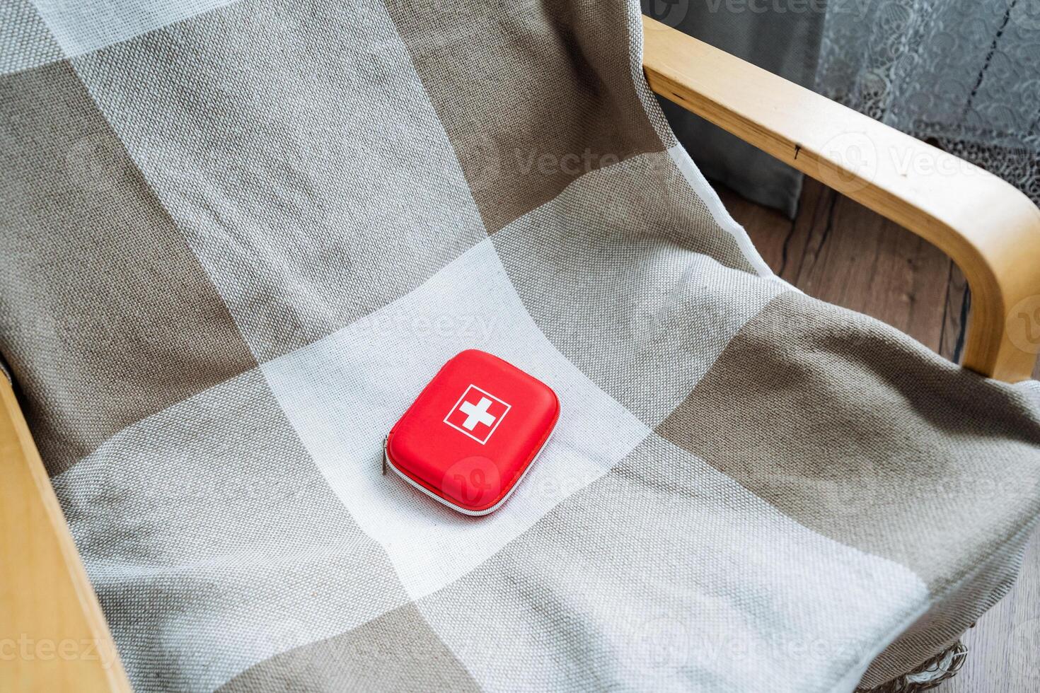 A vibrant red first aid kit sits prominently on a comfy chair that is covered with a soft plaid blanket, which adds warmth and creates an inviting and welcoming atmosphere for all photo