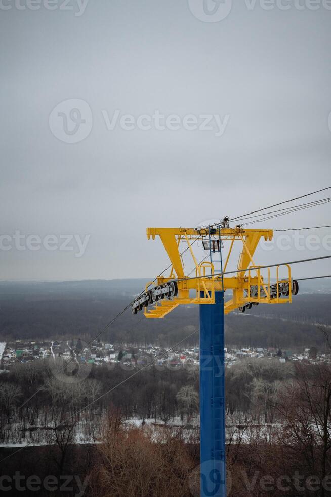 A bright yellow and blue ski lift ascends a snowy slope, providing breathtaking views of the landscape in the morning sunlight under a clear blue sky, supported by sturdy poles photo