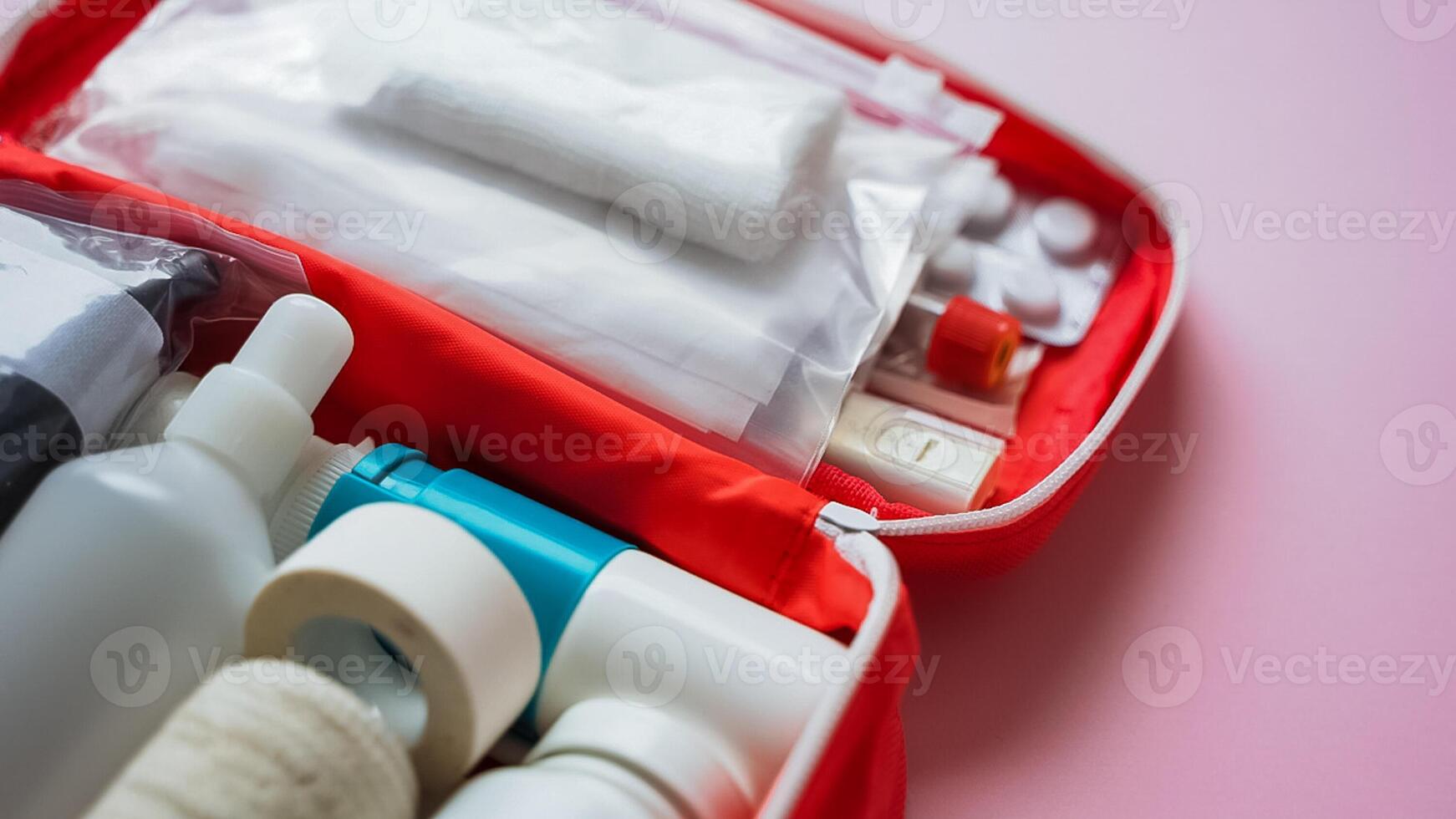 A vibrant red first aid kit is generously filled with various bottles and pills, all resting on a soft pink surface, showcasing a rich and inviting contrast of colors and textures photo