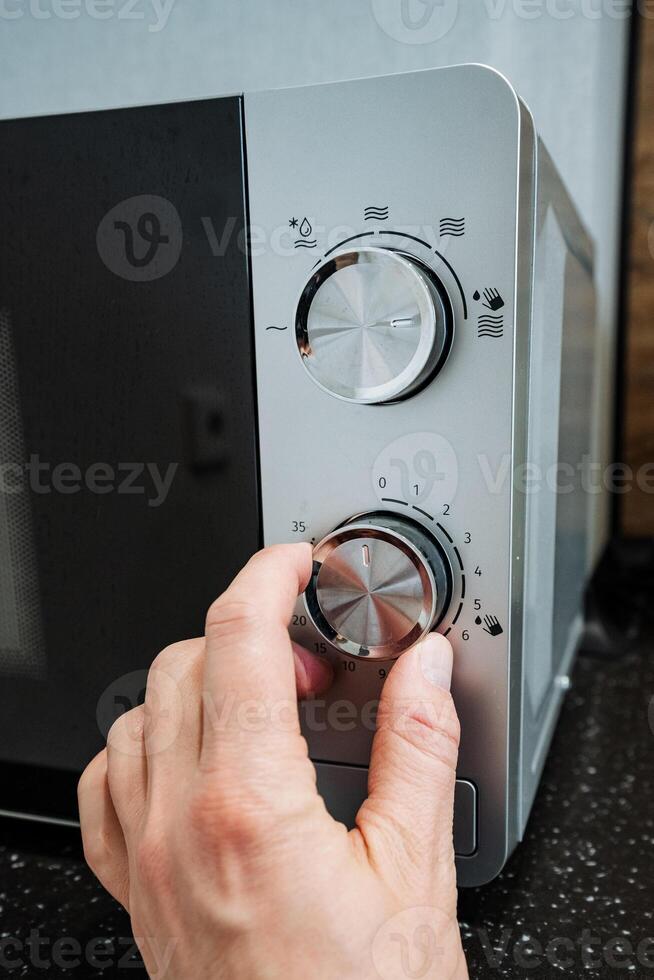 A person is turning a knob on a microwave, which is a widely used kitchen appliance known for its ability to efficiently heat and cook food while maintaining both flavor and texture photo