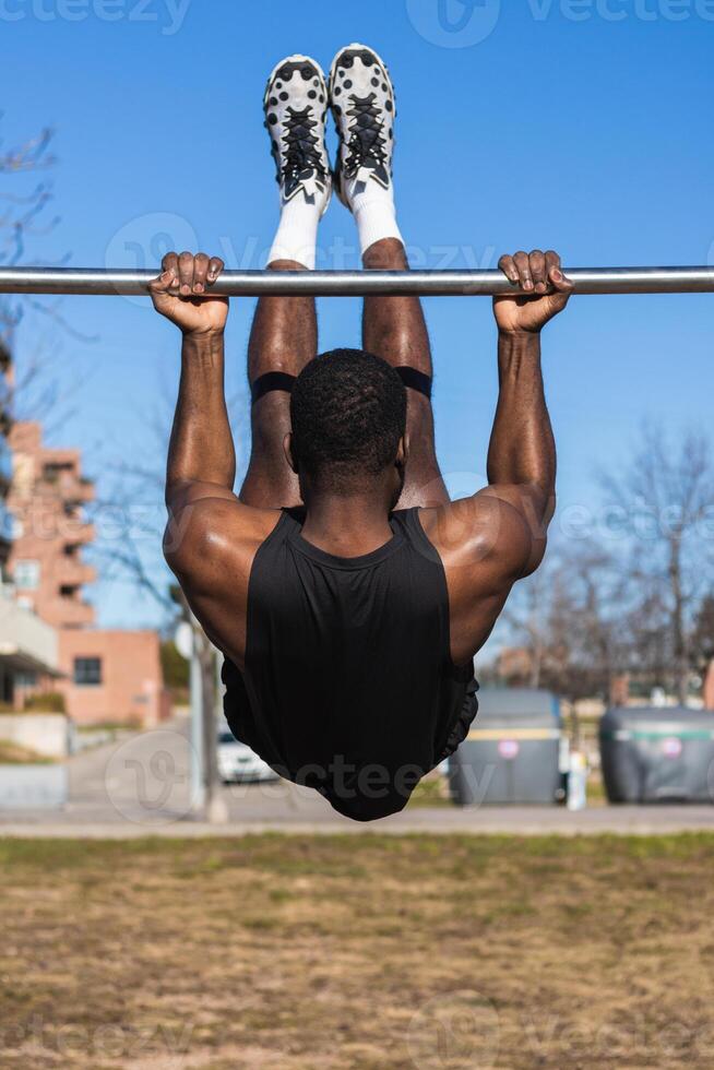 Unrecognizable strong black sportsman working out on bar in town photo