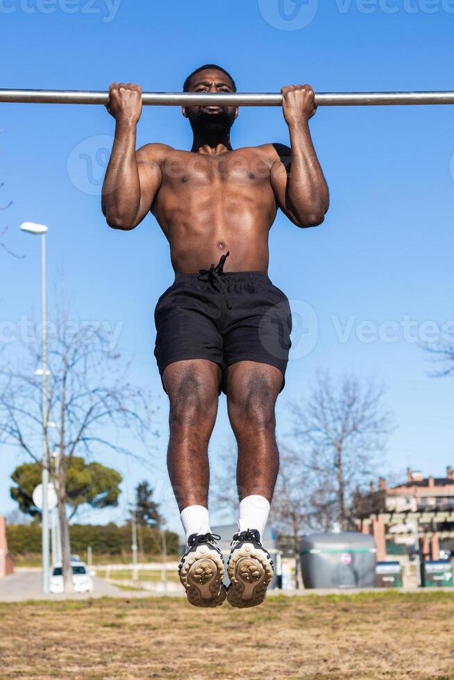 Strong black sportsman working out on bar in town photo