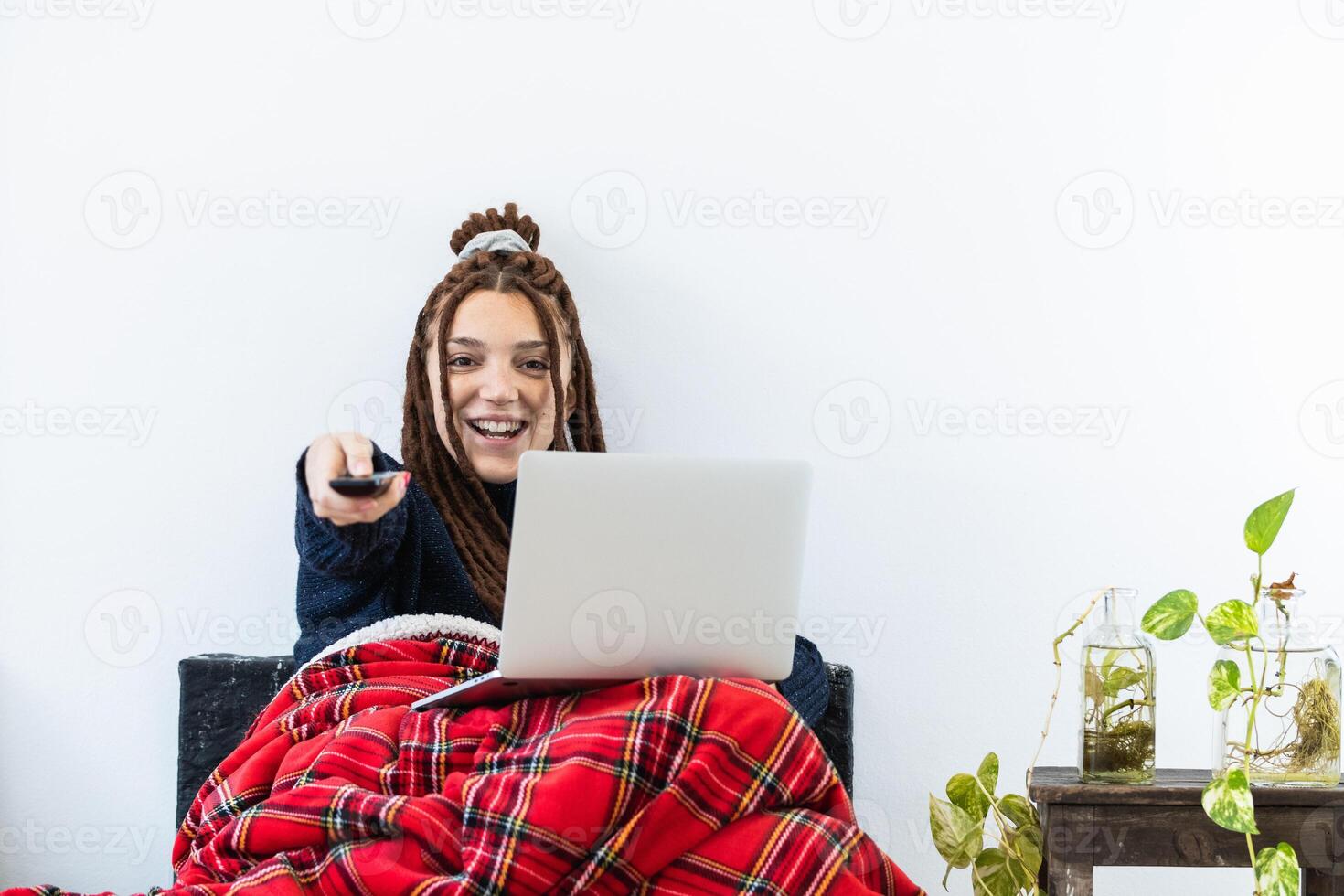 Woman with dreadlocks working with a laptop at home and with a remote control in hand photo