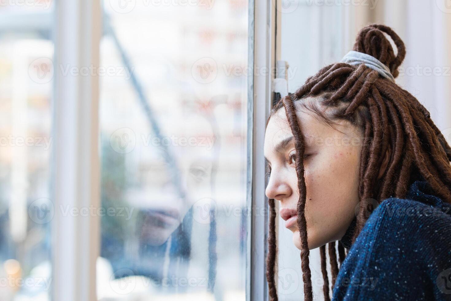 Pensive woman with dreadlocks looking out the window photo