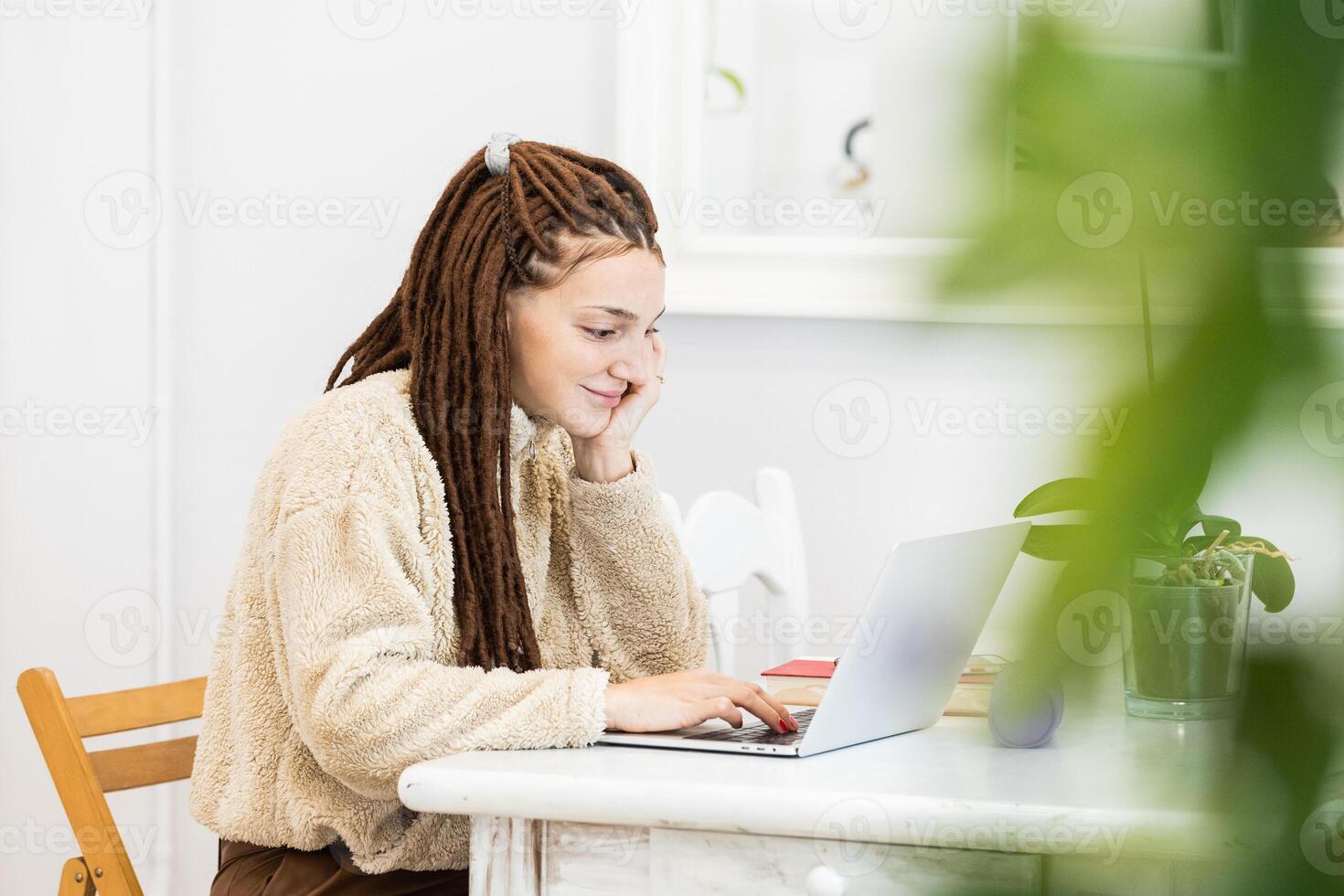 Thoughtful woman with dreadlocks working with a laptop at home photo