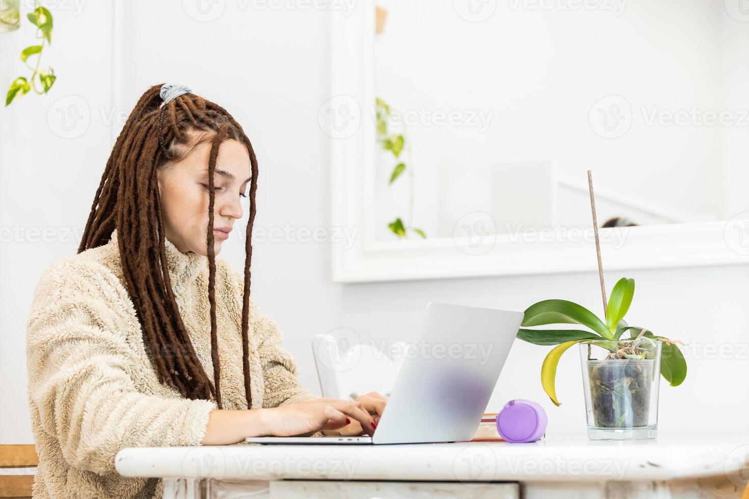 Thoughtful woman with dreadlocks working with a laptop at home photo