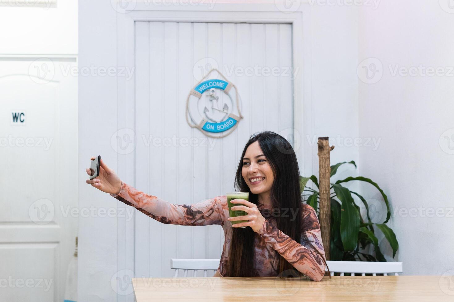 Smiling woman taking self portrait on smartphone at table in bar photo