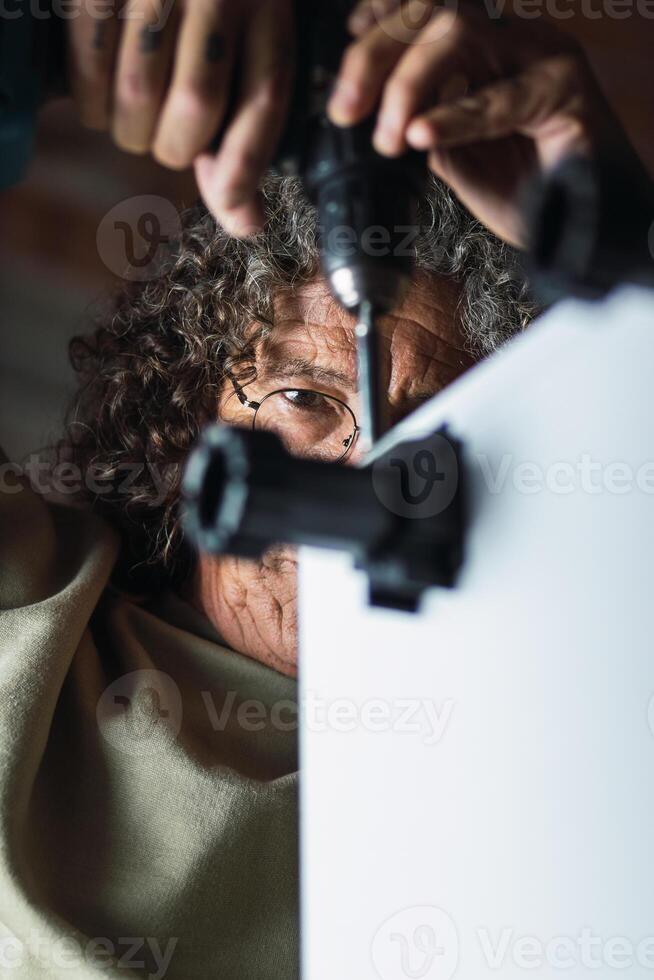 Focused elderly craftsman fixing plinth legs to cabinet working in studio photo