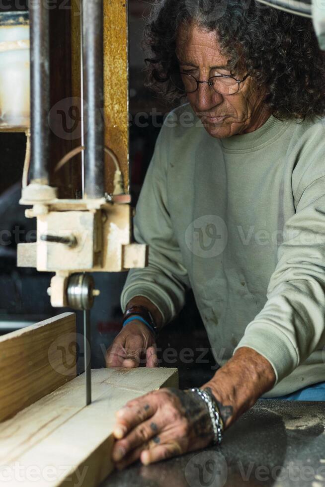 Mature male woodworker cutting plank with band saw photo