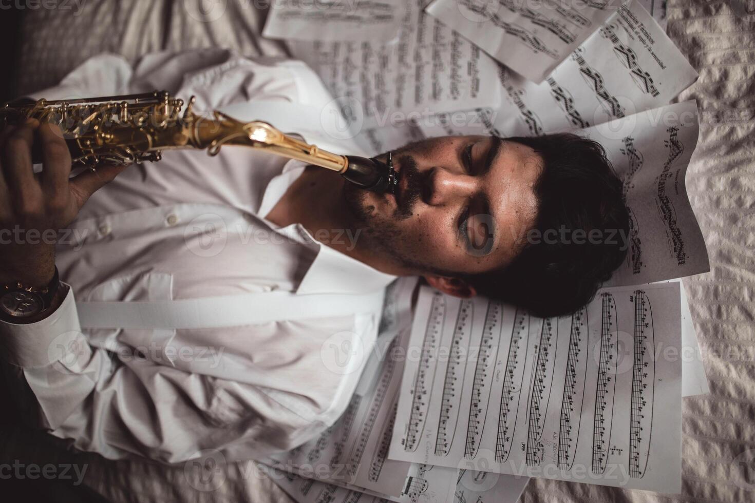 A man in a white shirt is laying on a bed with sheet music photo