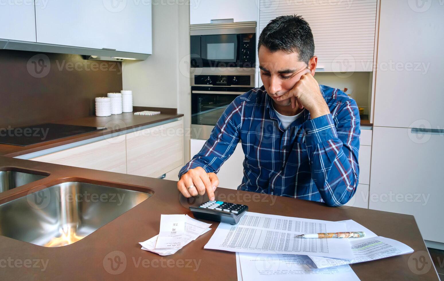 A man sitting at a kitchen table with a calculator photo