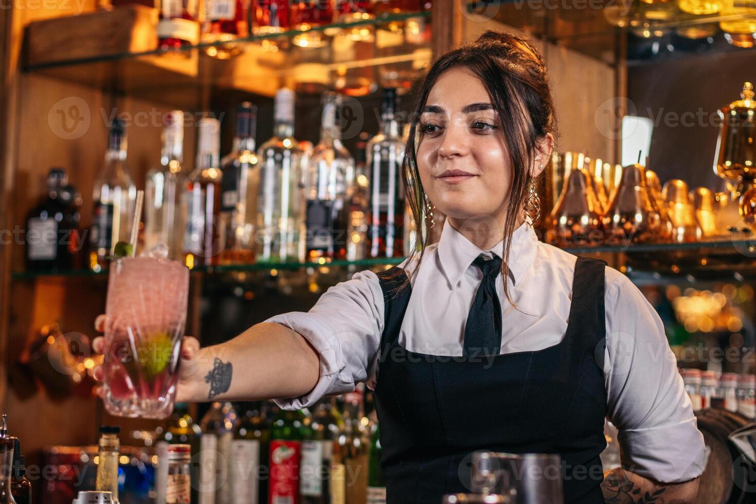 Young bartender offering a drink at the bar of a cocktail bar photo