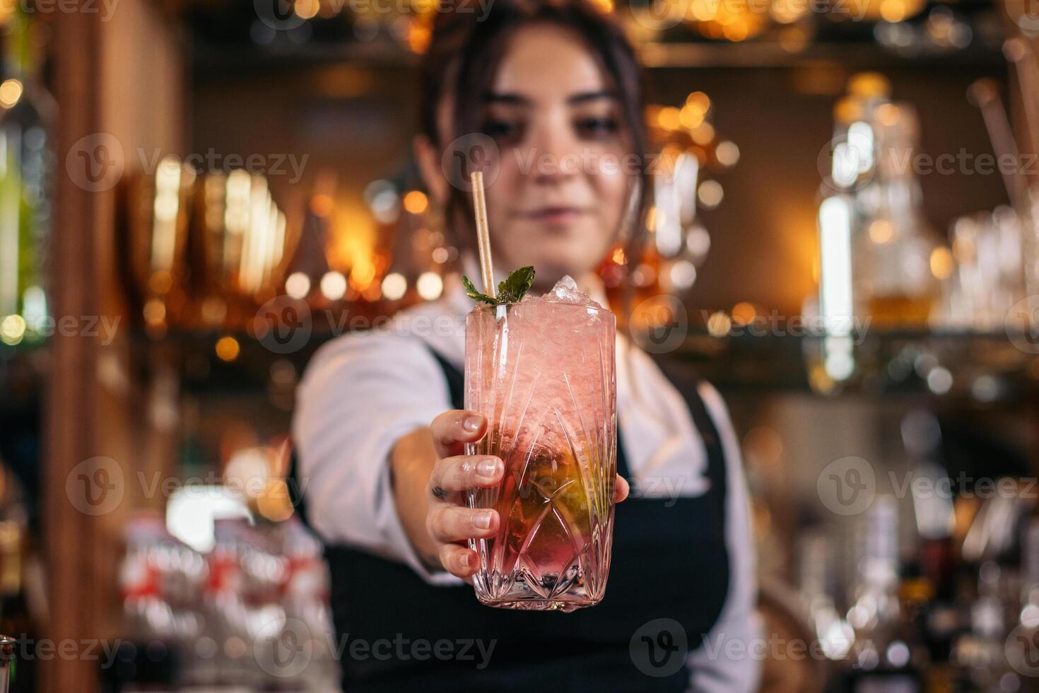 Young bartender offering a drink at the bar of a cocktail bar photo