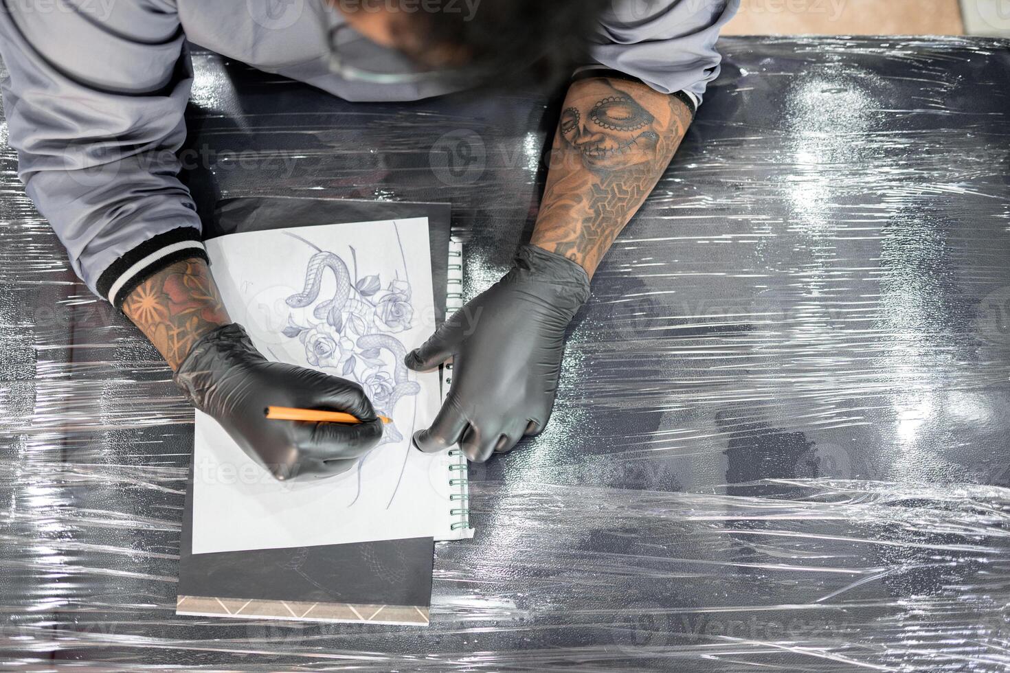 A tattoo artist is drawing a design stencil on his work stretcher before tattooing photo