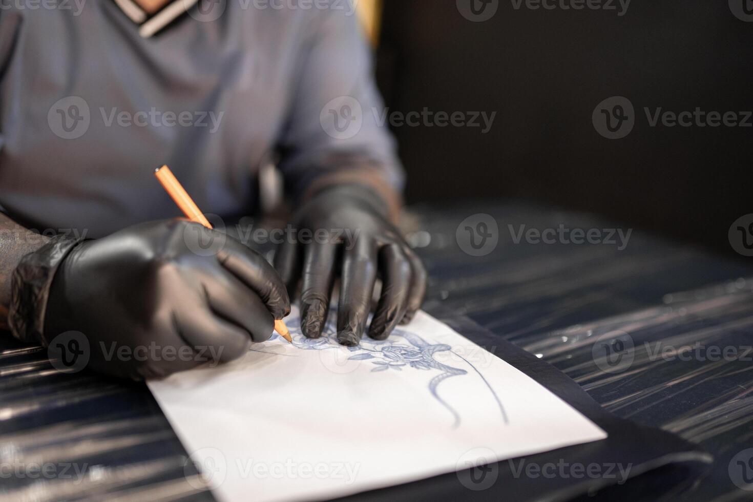 A tattoo artist is drawing a design stencil on his work stretcher before tattooing photo