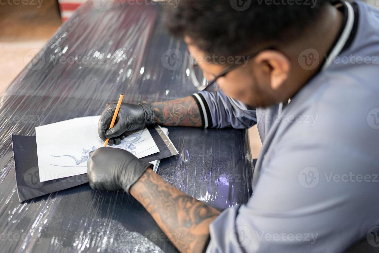 A tattoo artist is drawing a design stencil on his work stretcher before tattooing photo