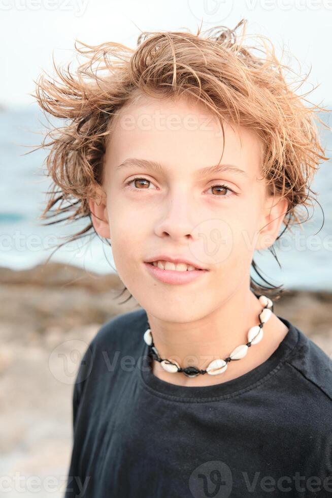Boy wearing shell necklace looking at camera at beach photo