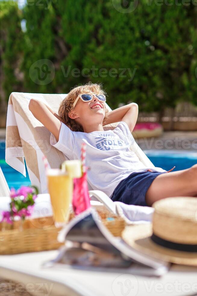 Boy with hands behind head relaxing on lounger at poolside photo