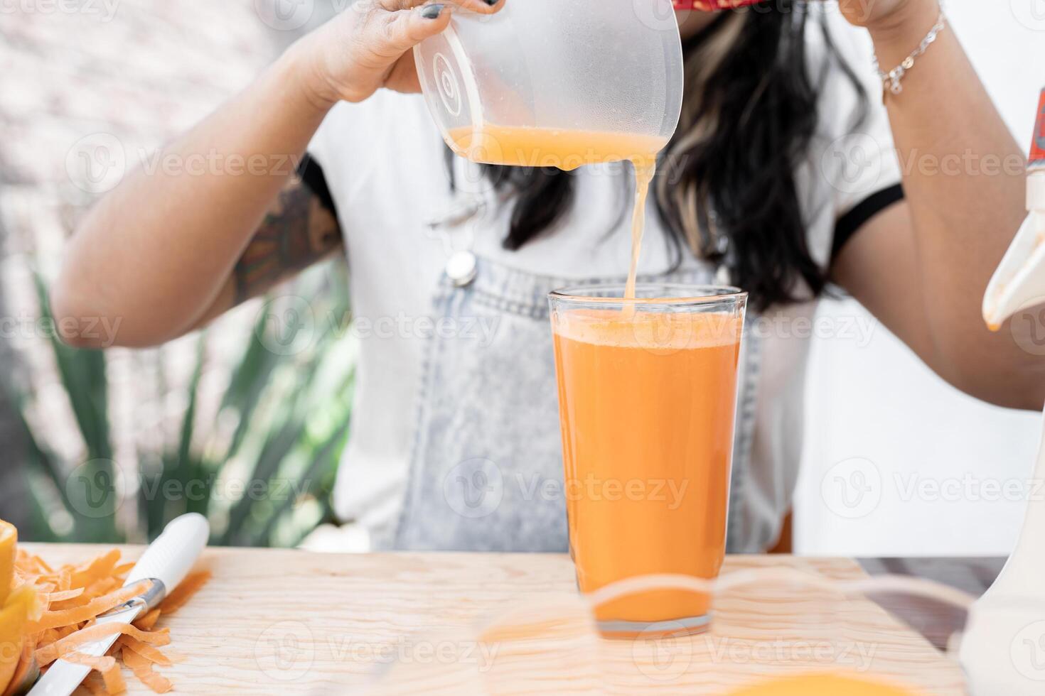A young Hispanic woman is mixing fresh squeezed orange and carrot juice in a glass photo