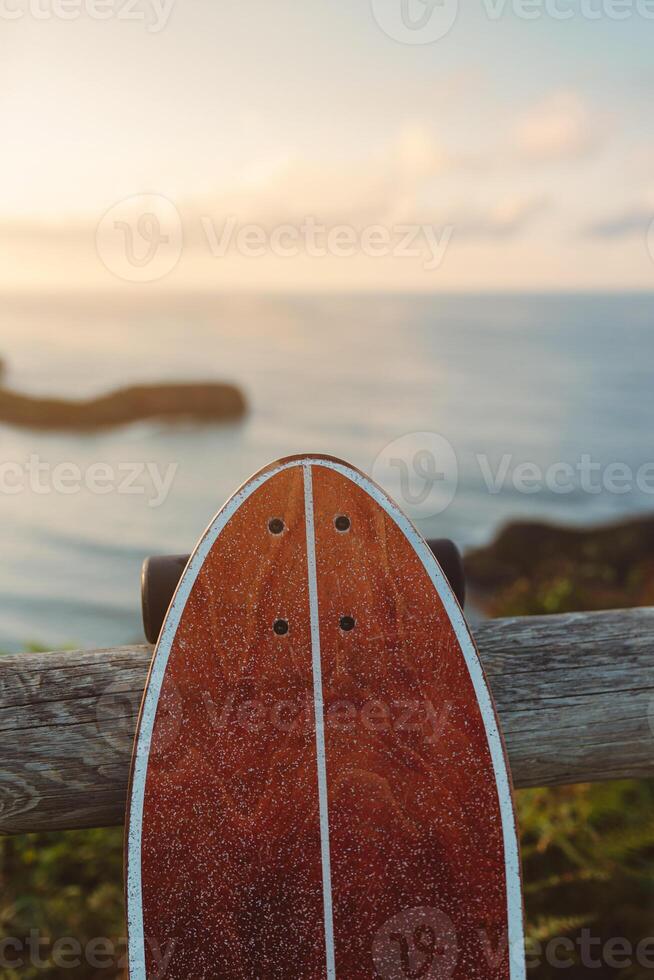 Surf skate leaning on wooden railing against blurred beach photo