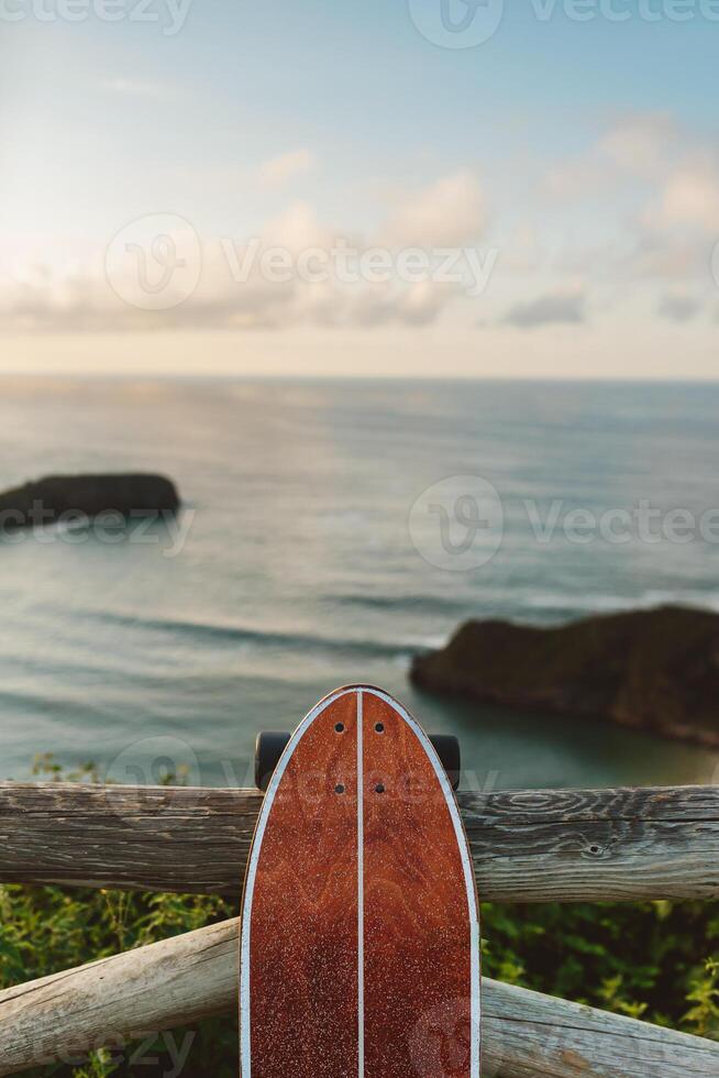 Surf skate leaning on wooden railing against blurred beach photo