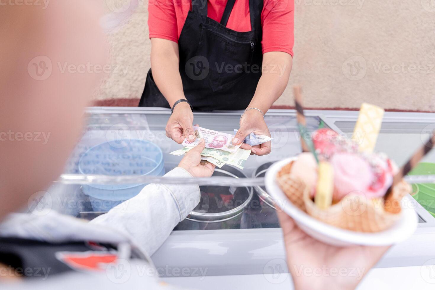 A young Hispanic woman is waiting for her change while holding a big traditional Mexican ice cream photo