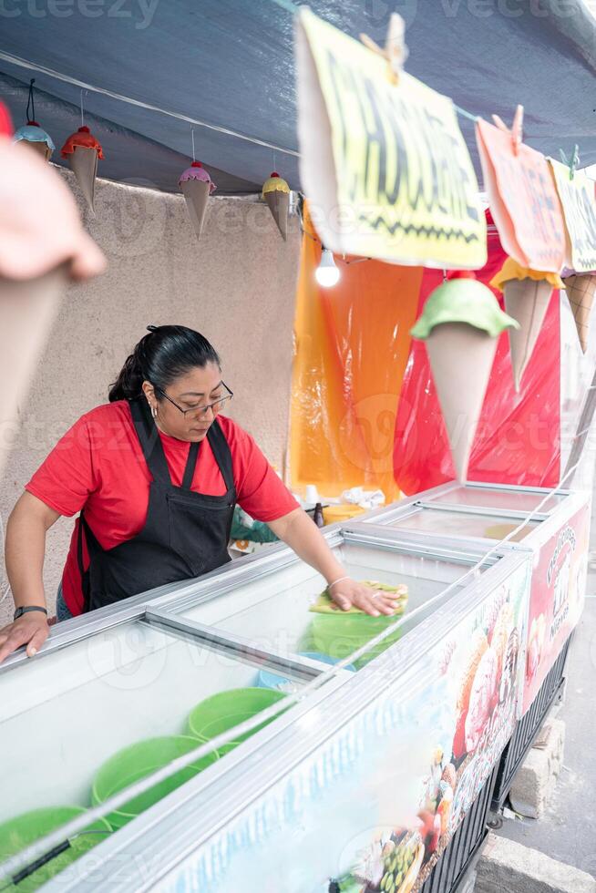 An Hispanic woman is cleaning the ice cream freezer in her street market stall photo