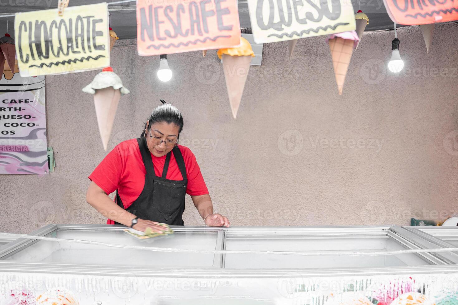 An Hispanic woman is cleaning the ice cream freezer in her street market stall photo