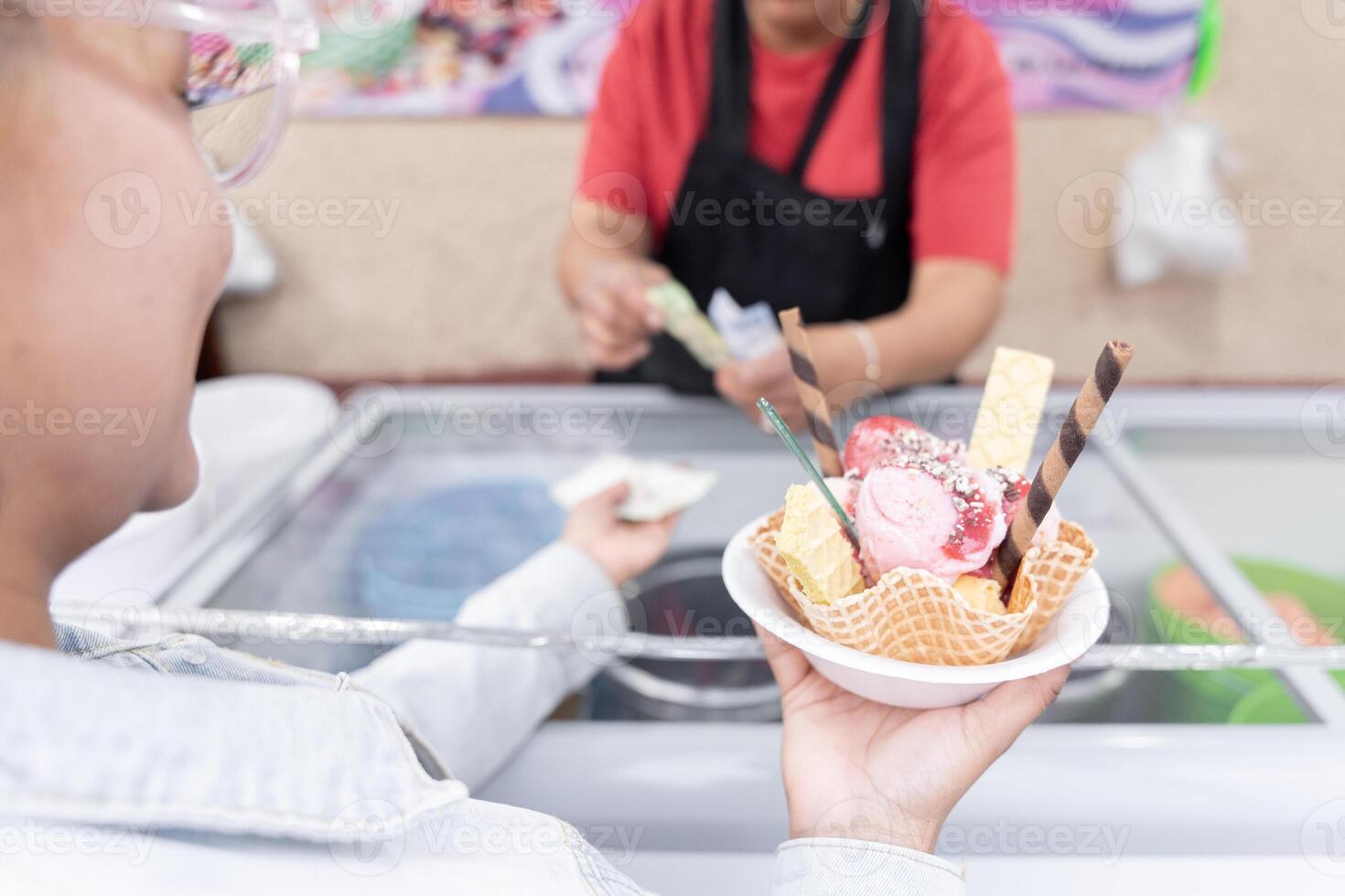 A young Hispanic woman is waiting for her change while holding a big traditional Mexican ice cream photo