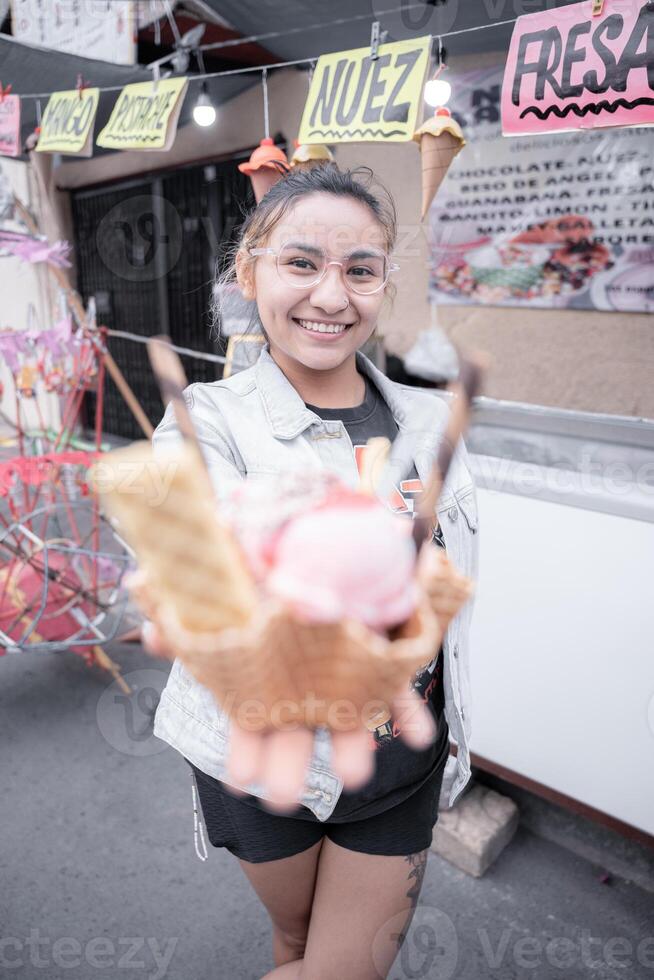 A young Hispanic woman is smiling holding a traditional ice cream in front of a street market stall photo