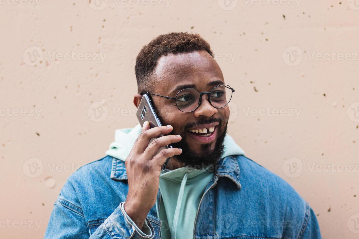 Cheerful black man talking on phone near wall photo