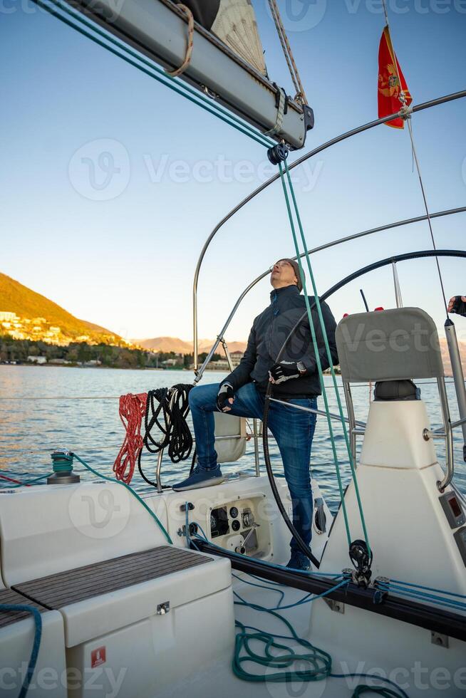 Young man captain standing at helm and controls sailboat during a journey by sea in winter time in Montenegro photo