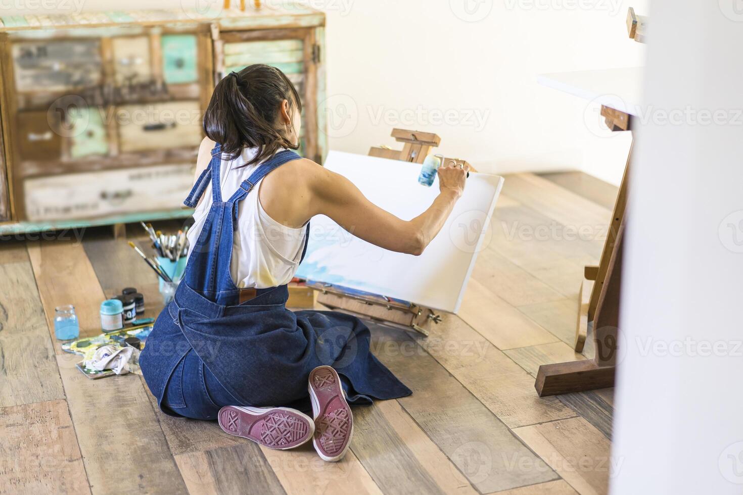 A woman sitting on the floor painting on a canvas photo