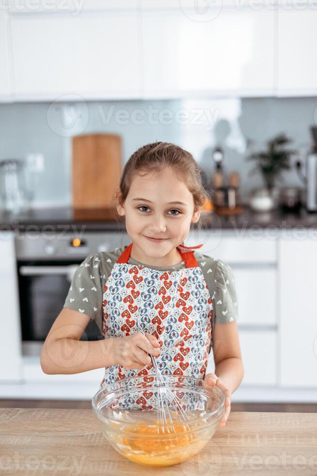 A little girl in an apron mixing up a bowl of orange juice photo