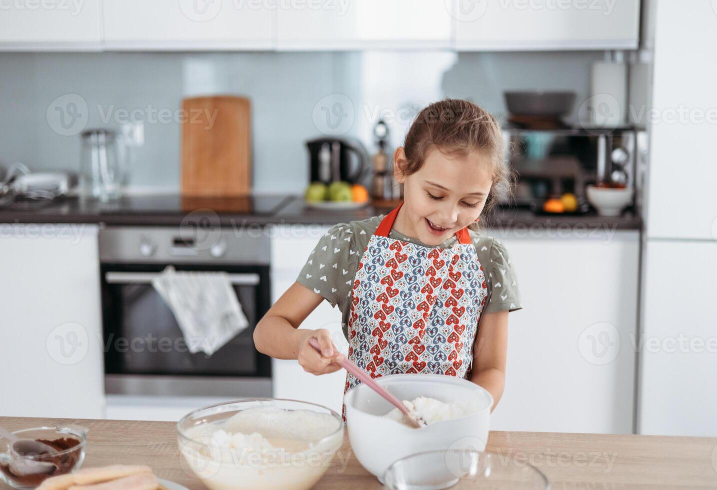 A little girl in an apron mixing ingredients in a bowl photo