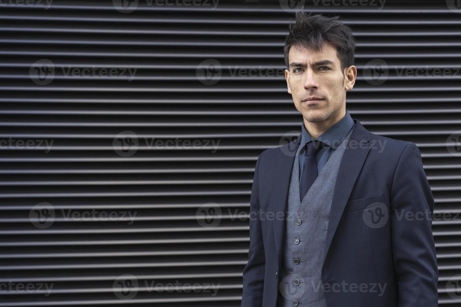 A man in a suit and tie standing in front of a wall photo
