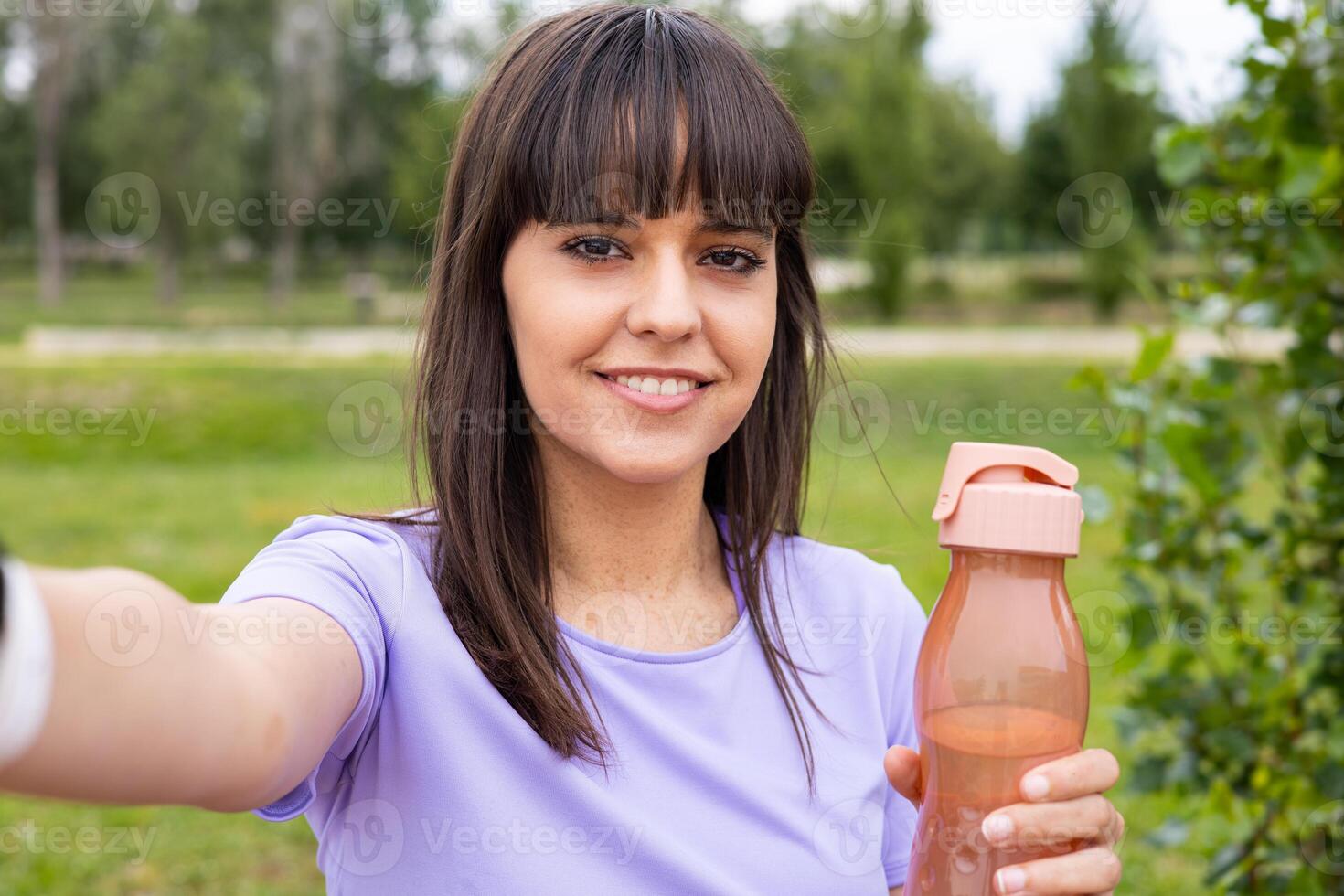 A woman is holding a water bottle and taking a selfie photo