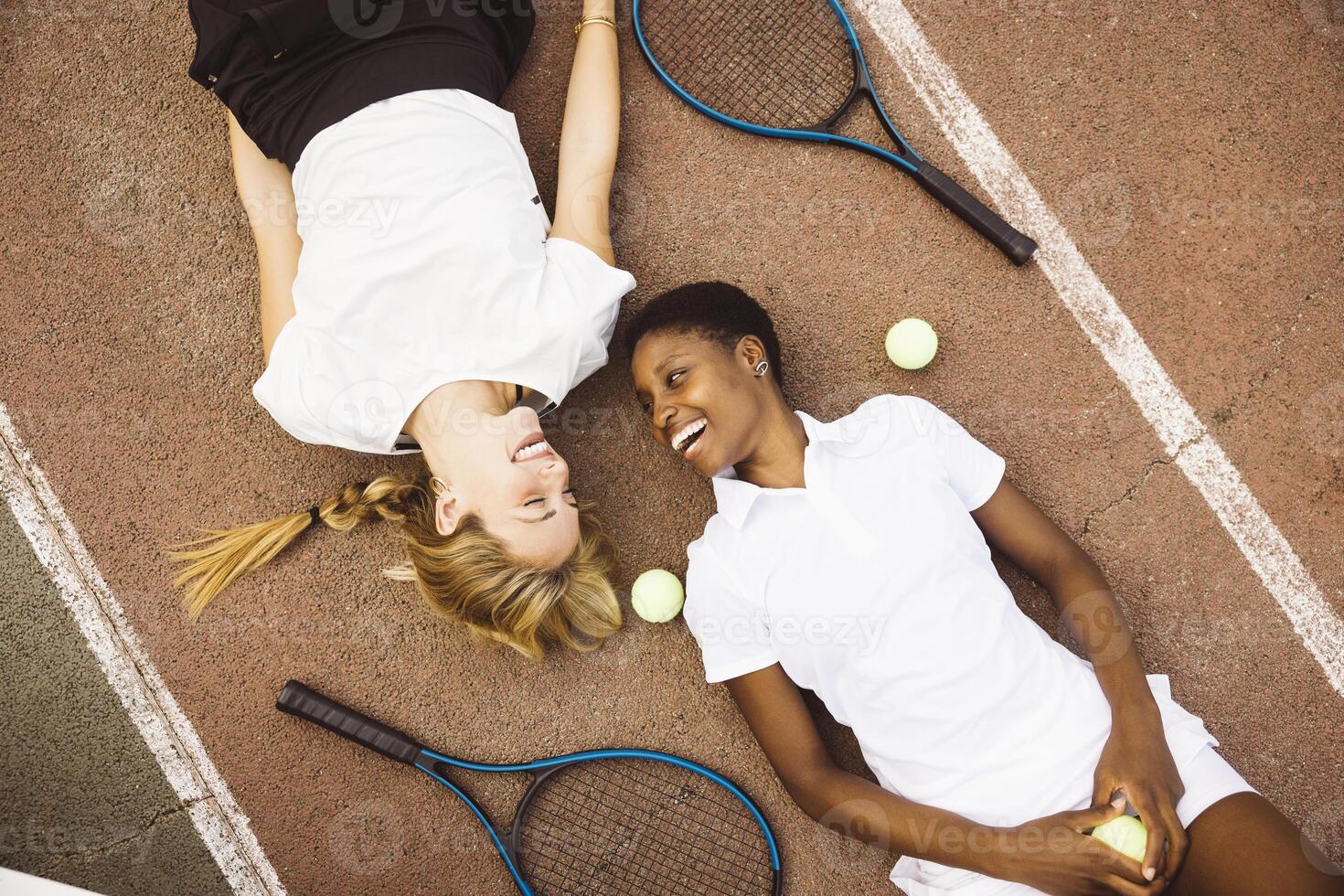 Two women laying on the ground with tennis rackets photo
