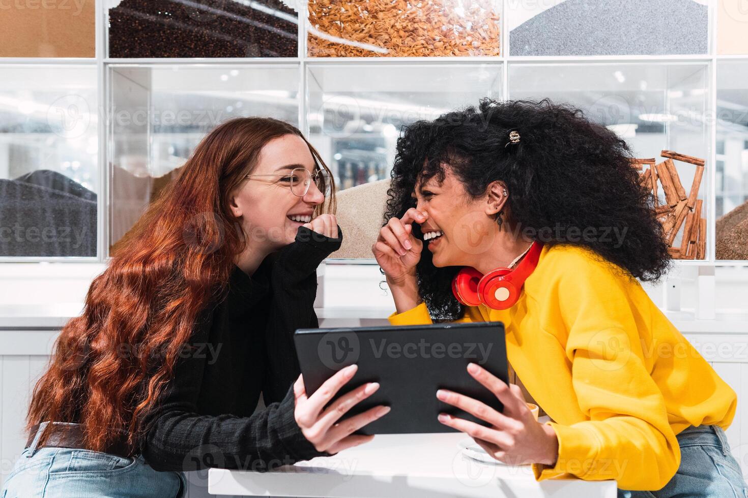 Positive multiethnic female friends using tablet and laughing in cafe photo