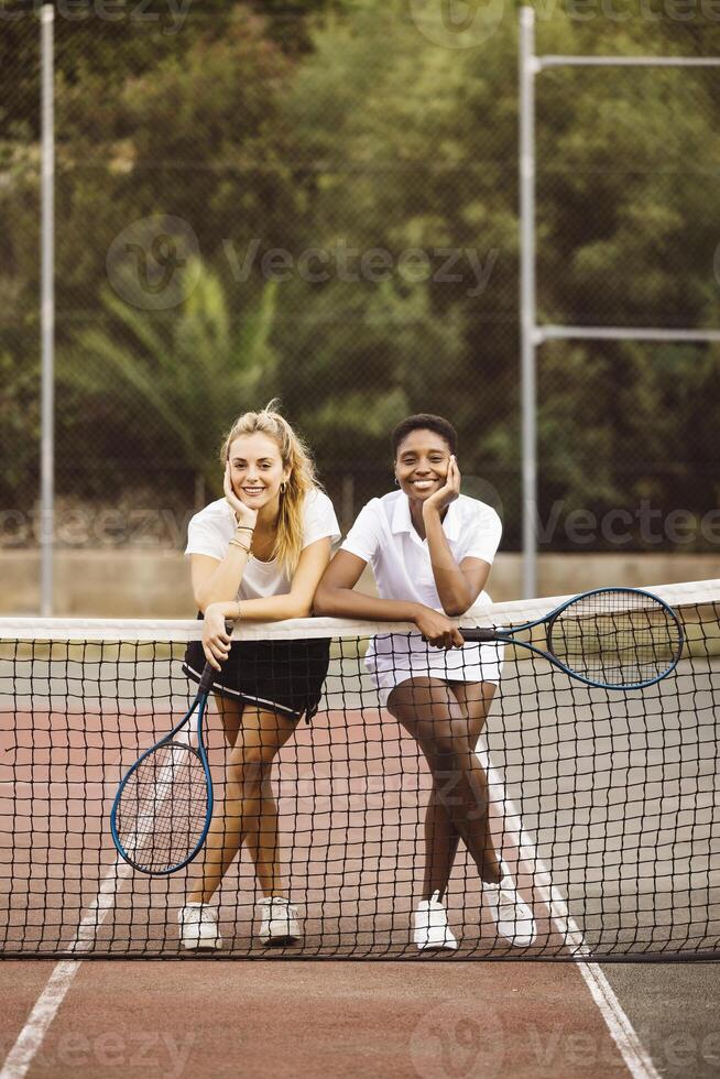 Two women posing with tennis rackets on a tennis court photo