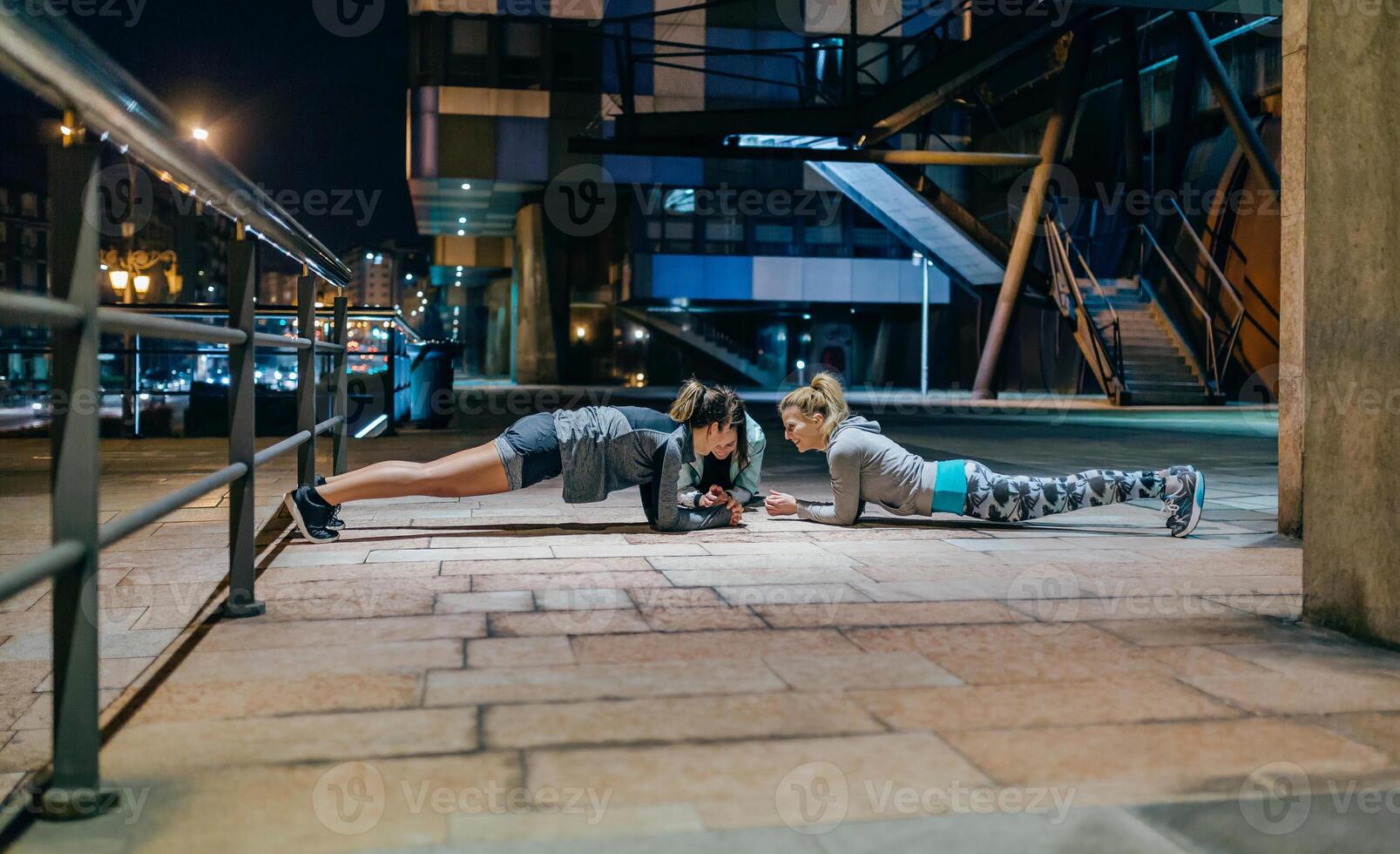 Two women doing push ups on a sidewalk at night photo